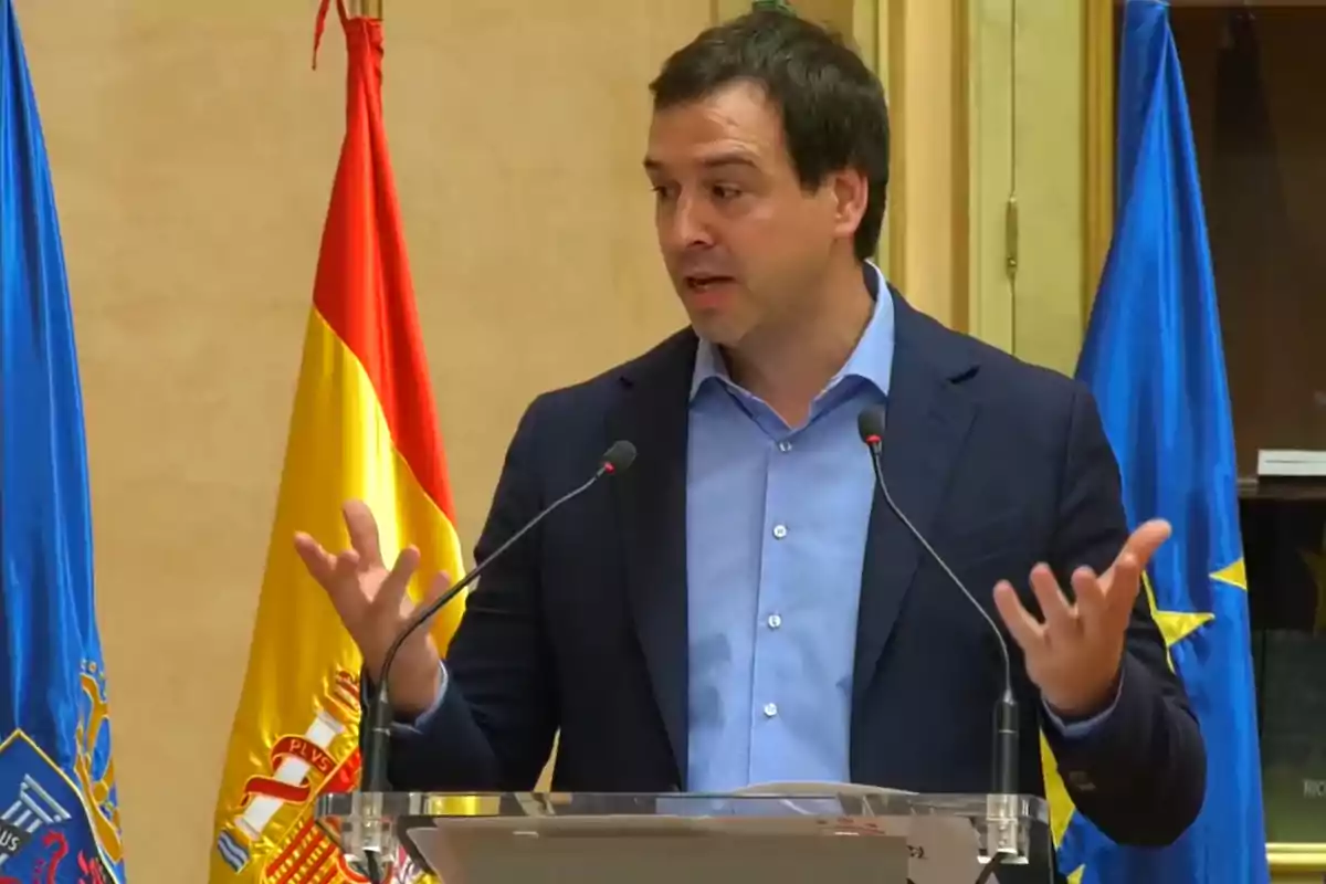 Un hombre hablando en un podio con banderas de España y la Unión Europea detrás. Un hombre hablando en un podio con banderas de España y la Unión Europea detrás.